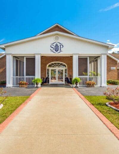 Direct view of pathway lined with bushes and grass leading to main entrance of Southern Pines Senior Living